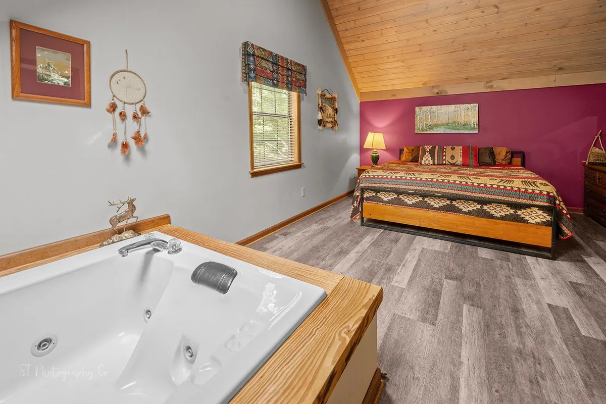 An inviting master suite with a jacuzzi tub, patterned bedding, colorful wall decor, and soft lighting that creates a tranquil, intimate atmosphere for unwinding after a busy day.