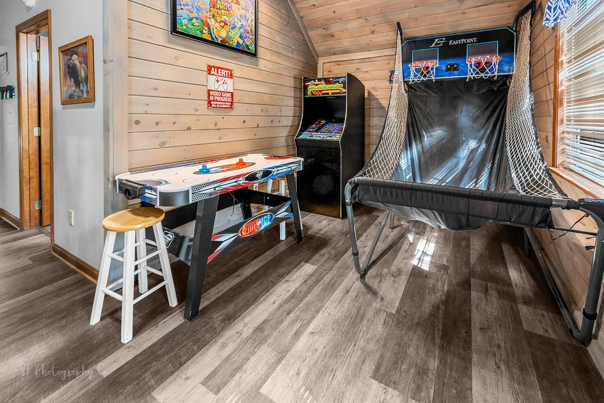 A game room with a retro arcade machine, air hockey table, and basketball arcade game. The space is decorated with colorful wall art, creating a fun and energetic mood perfect for bonding and laughter. Multiple activities can be seen in a single shot, appealing to families and groups.