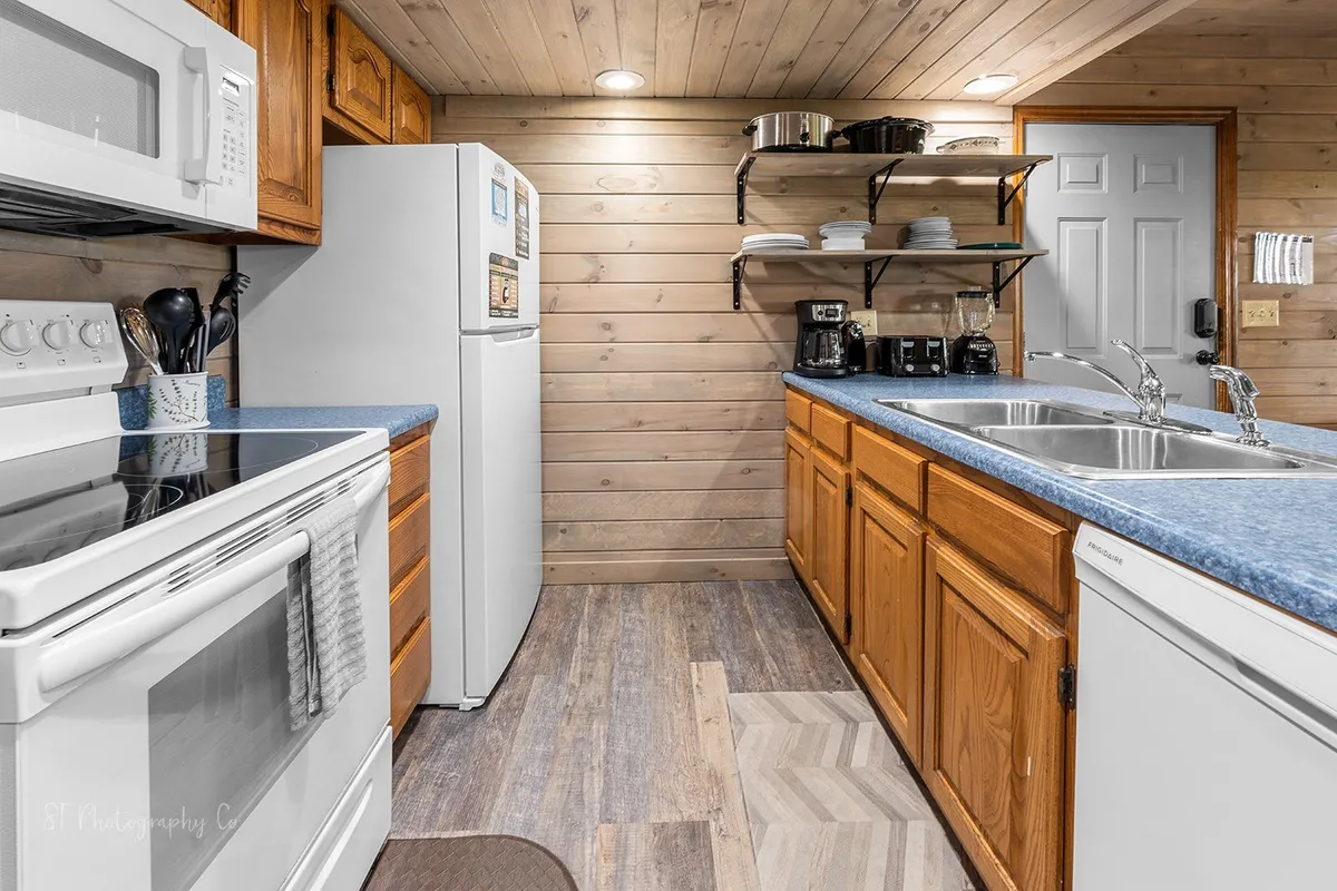A modern kitchen with stainless steel appliances, wooden cabinetry, a double sink, and ample countertop space. The kitchen feels warm and welcoming, ideal for cooking, chatting at the bar, or preparing group meals.
