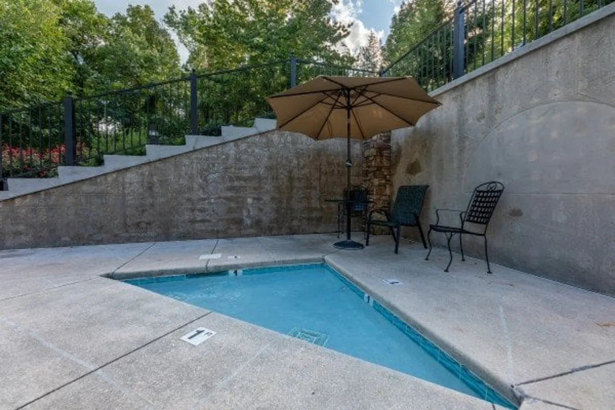 A serene exterior view of a smaller pool surrounded by chairs and an umbrella, set amidst lush greenery. The space is inviting for both relaxation and socializing, with a staircase leading to the pool area.
