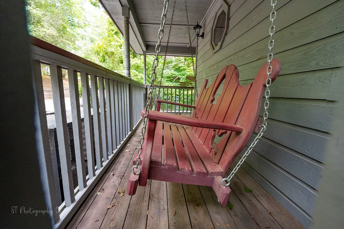This photo features a pair of inviting red swing chairs on a wooden porch, with a backdrop of dense greenery. The scene evokes peaceful moments spent relaxing, reading, or sipping morning coffee.