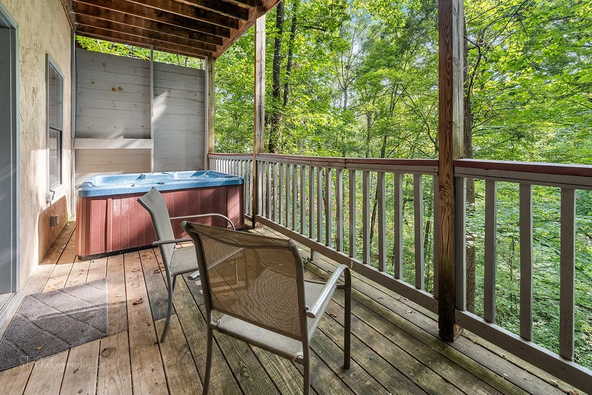 This exterior deck image features a bubbling hot tub, sturdy wooden railings, and lush trees providing a tranquil, private retreat. The scene is peaceful, ideal for stargazing or enjoying quiet family moments after a day out.