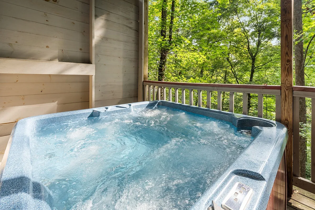 A serene exterior view of the hot tub set on a wooden deck, surrounded by lush trees. The tub is perfectly situated for soaking up the natural surroundings and enjoying sunset views in a tranquil, immersive environment.