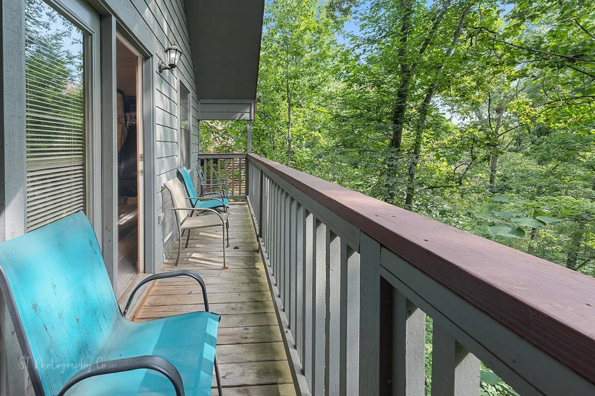 A cozy deck with turquoise chairs and a wooden railing facing out toward vibrant greenery. This inviting outdoor seating area is ideal for sipping coffee, birdwatching, or simply soaking up the seasonal mountain atmosphere.
