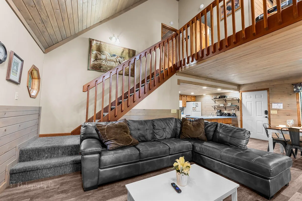 A spacious living room featuring a large sectional sofa arranged around a stone gas fireplace, with a visible staircase and artwork adding homely accents. The setting is cozy and inviting, perfect for family gatherings, relaxing by the fire, or enjoying games.