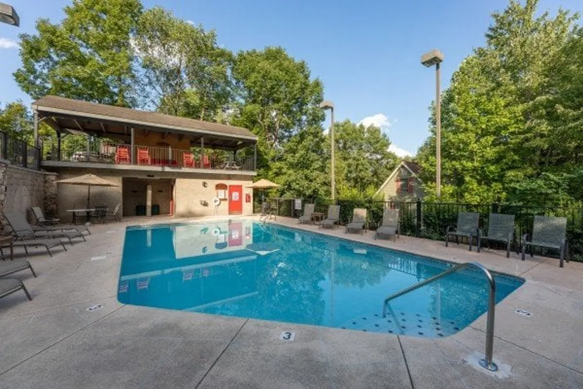 This image shows a large outdoor swimming pool with a poolside deck, lounge chairs, and a clubhouse in the background. The setting is perfect for group gatherings, community events, or simply relaxing and socializing in a sun-filled environment.