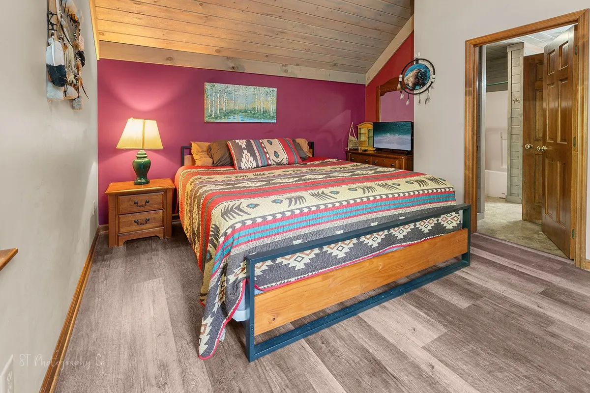 A sun-filled bedroom with a bed dressed in a colorful blanket, a wooden bedside table with a lamp, and vibrant artwork adorning the wall. The space feels inviting and restful, perfect for unwinding after a day outdoors.